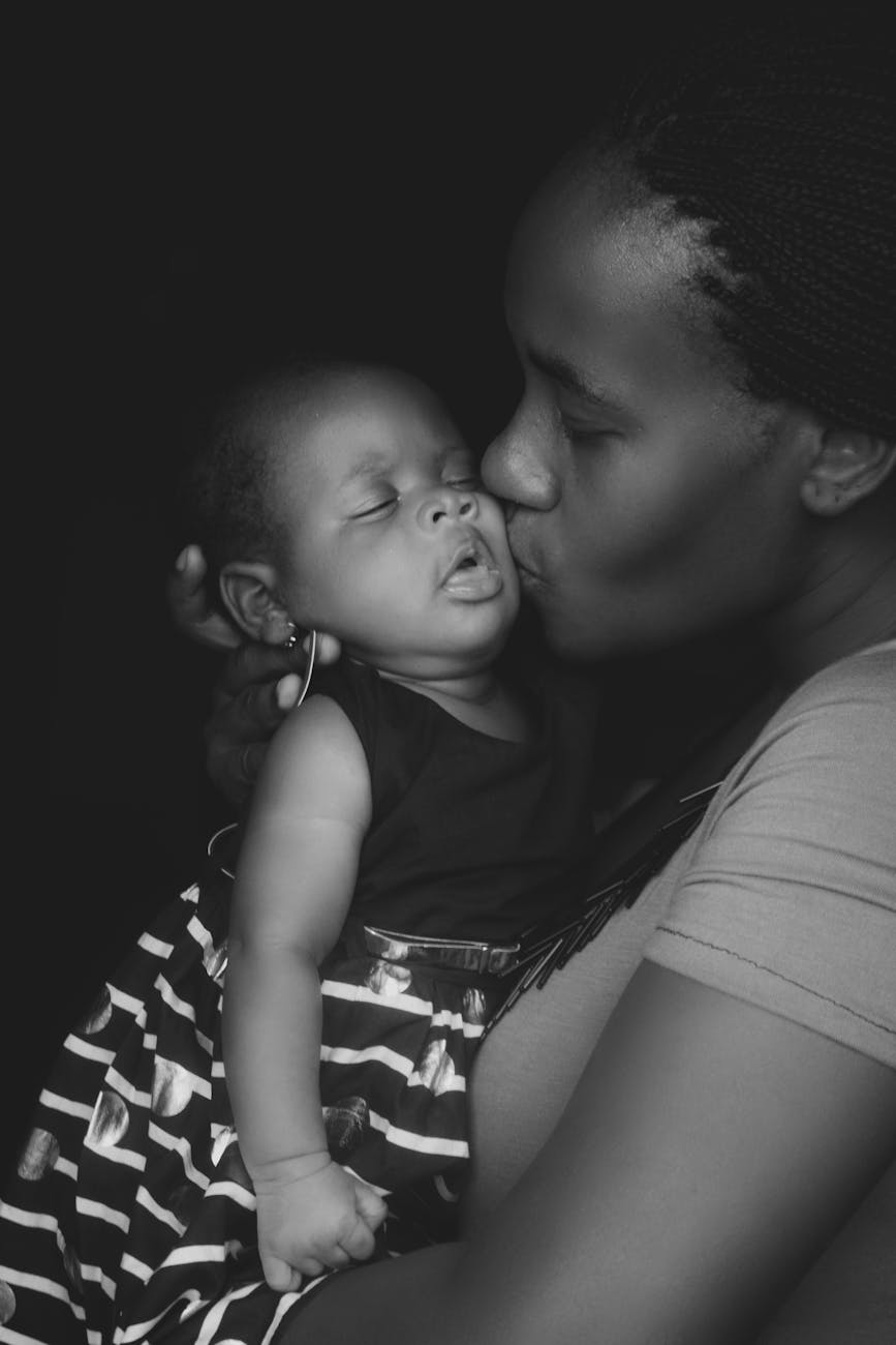 grayscale photo of mother kissing her baby