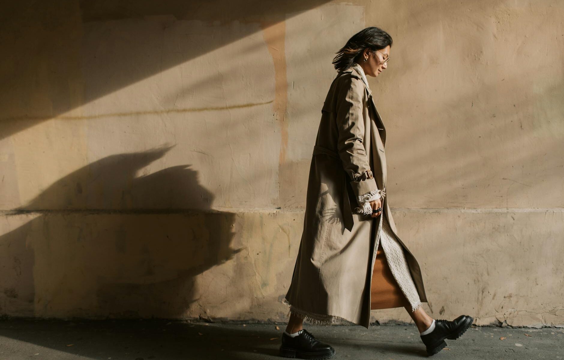 woman wearing trench coat walking near a wall